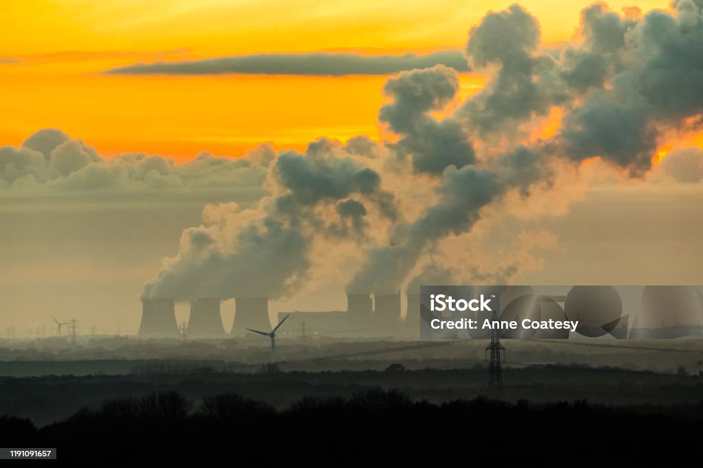 The imposing cooling towers of a power station near the village of Drax in North Yorkshire.  Plumes of water vapor leave a trail in the cold November night air.   Horizontal.  Space for copy.